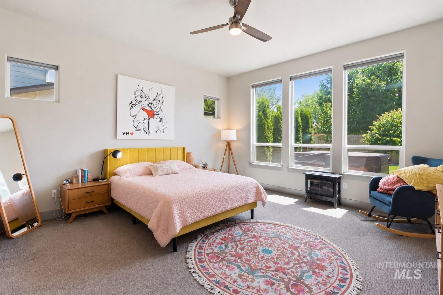 Carpeted room featuring a ceiling fan, a wall-mounted heating unit, and multiple windows