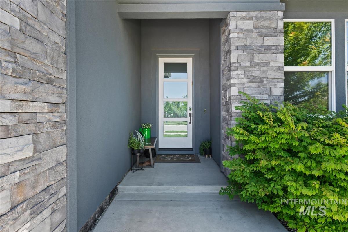 Entryway featuring a white door with multiple glass panes, stone veneer accents, stucco siding, concrete porch, and established shrubbery