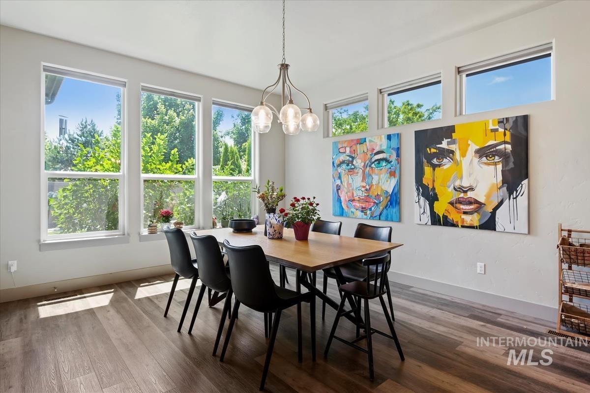 Spacious room featuring abundant natural light from multiple windows, wood-finish flooring, a contemporary chandelier, and high ceilings