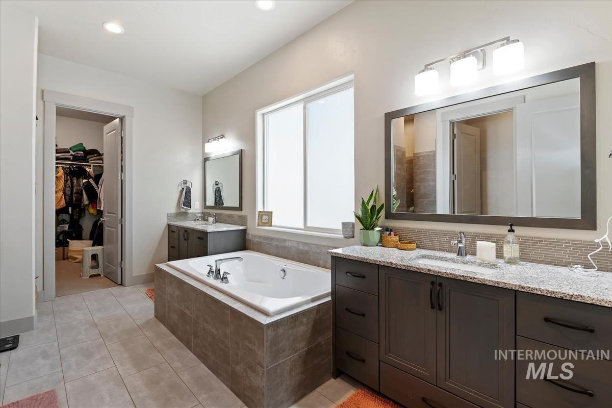 Spacious bathroom featuring an integrated soaking tub, dual vanity with granite-style countertops, and tile flooring