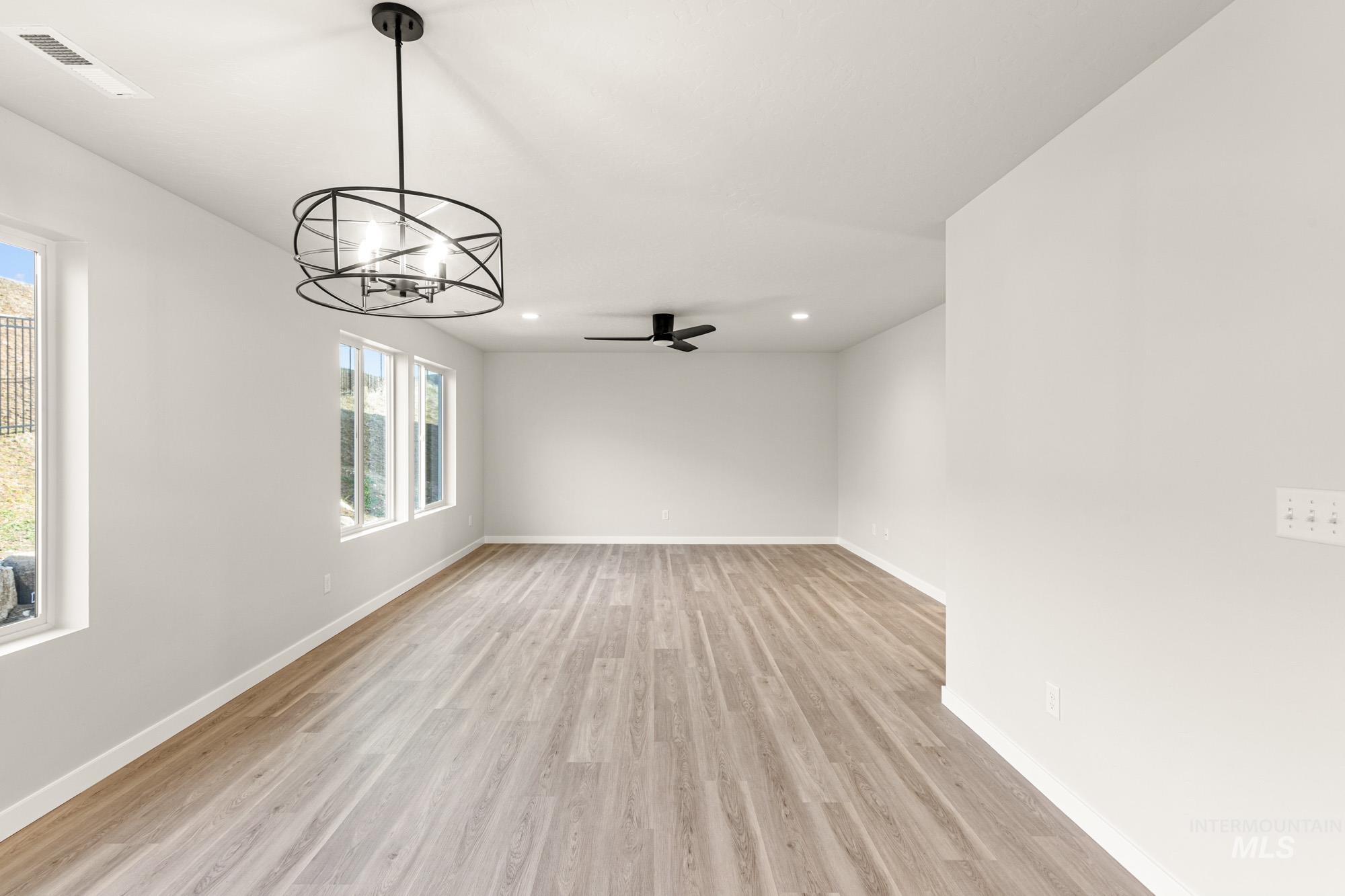Spare room with suspended lighting, light wood-style floors, and ceiling fan