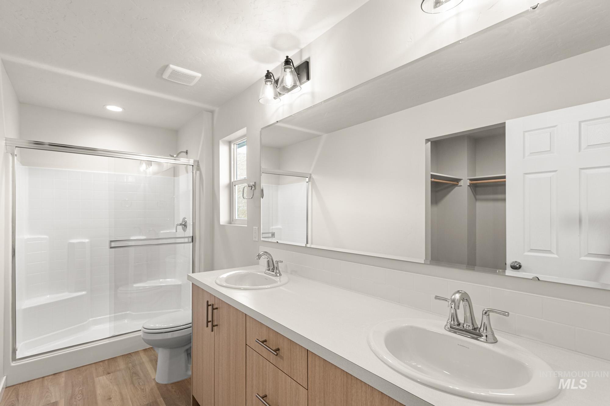 Bathroom featuring double vanity, a stall shower, light wood-type flooring, a walk in closet, and recessed lighting