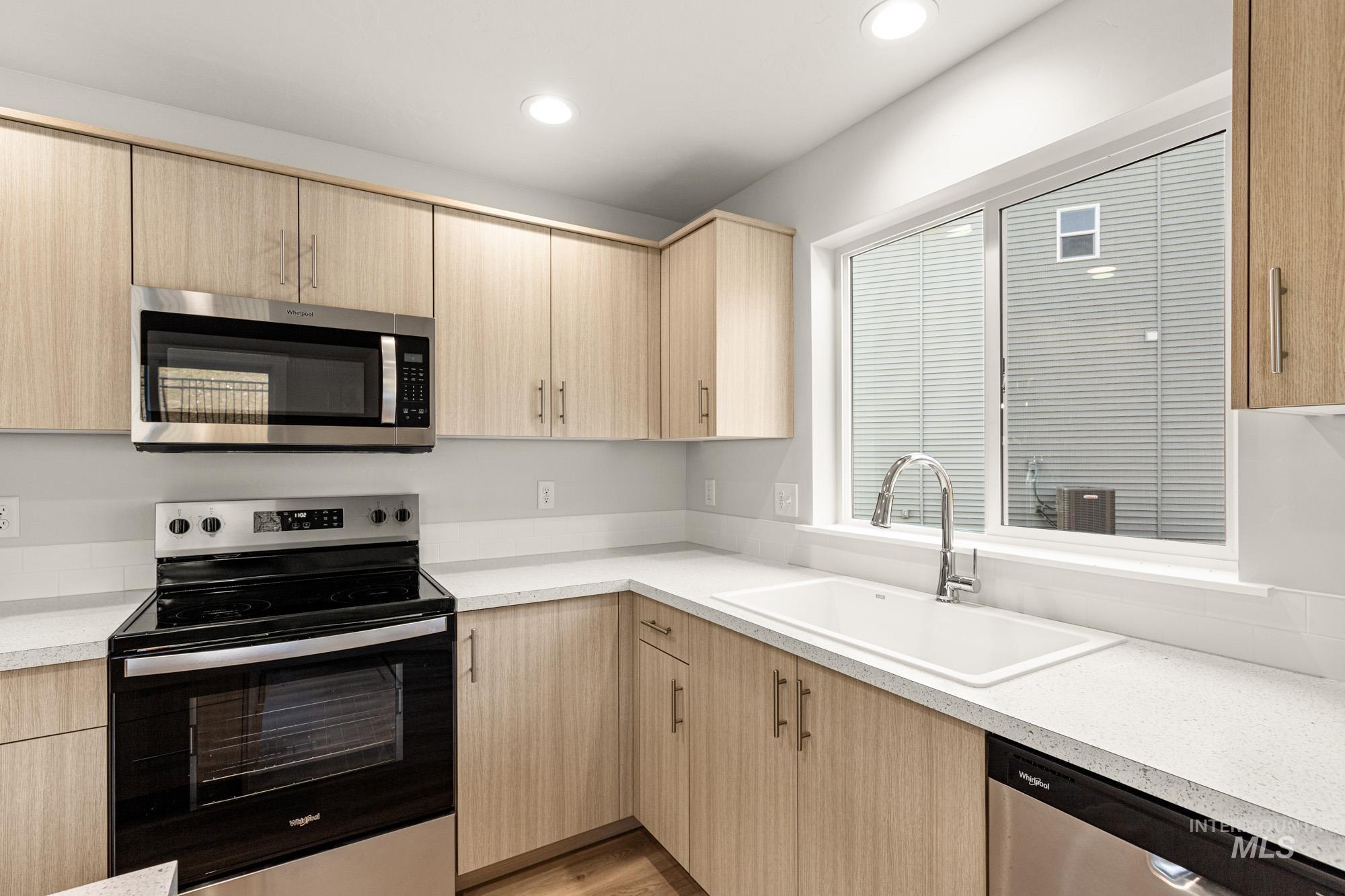 Kitchen with stainless steel appliances, light countertops, light wood finish cabinets, light wood-style floors, and recessed lighting