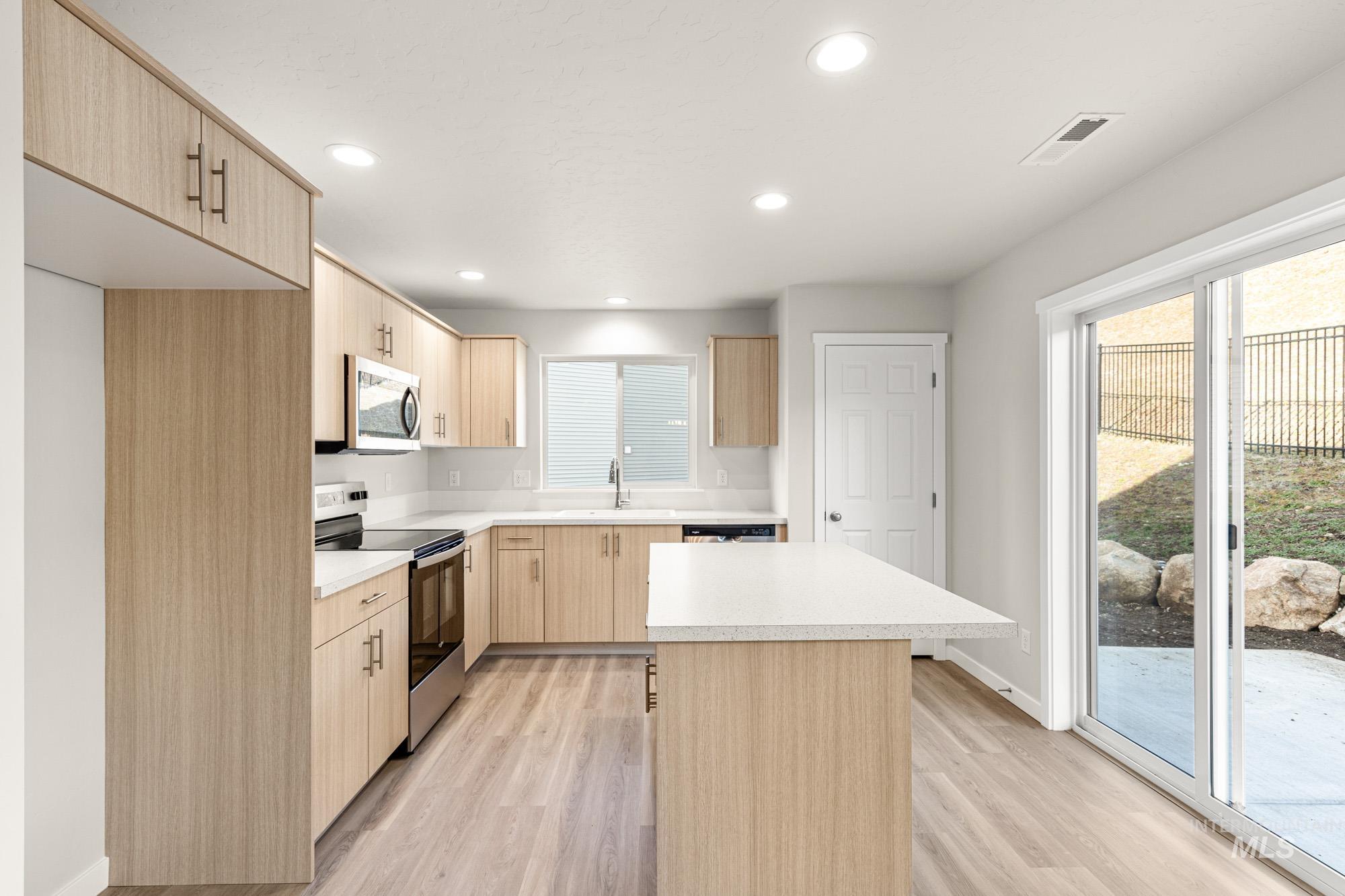 Kitchen featuring a kitchen island, light wood finish cabinets, stainless steel appliances, light countertops, and recessed lighting