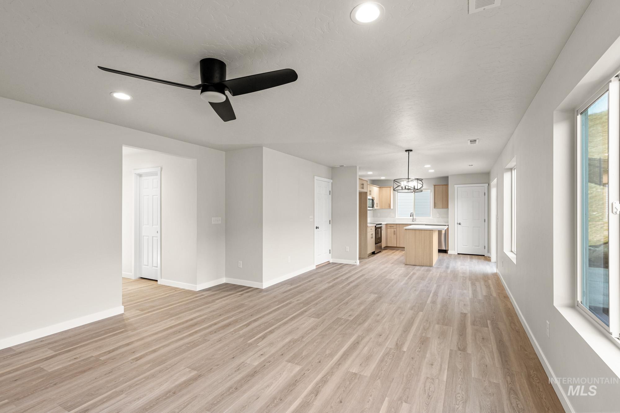 Unfurnished living room featuring light wood-style floors, a ceiling fan, and a chandelier