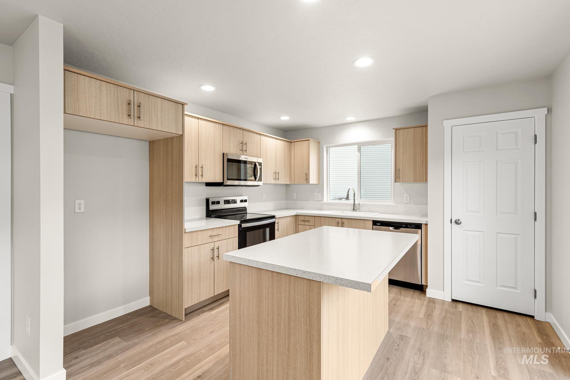 Kitchen with stainless steel appliances, light countertops, light wood-type flooring, a kitchen island, and recessed lighting