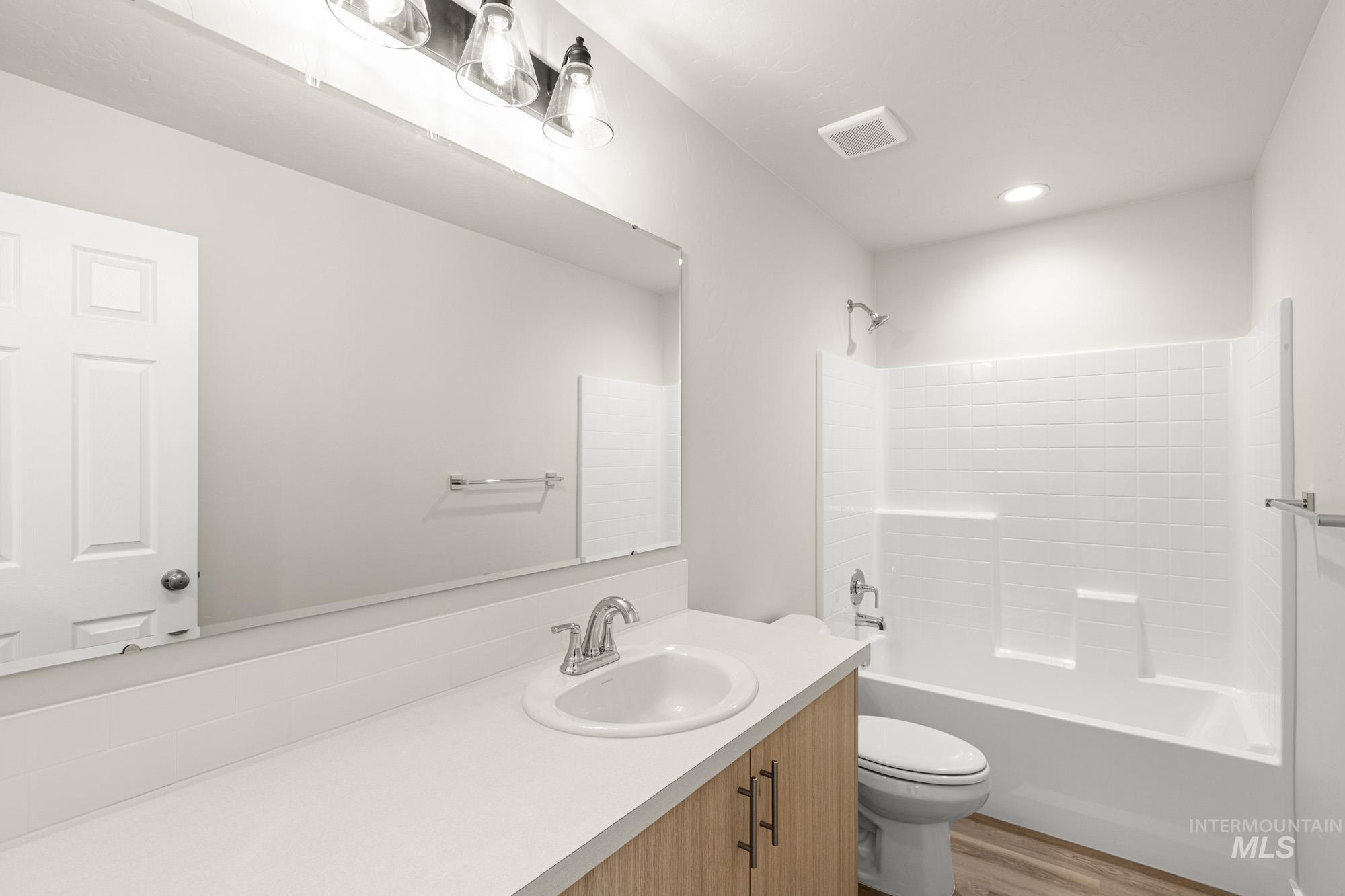 Full bathroom with vanity, washtub / shower combination, and light wood-style floors