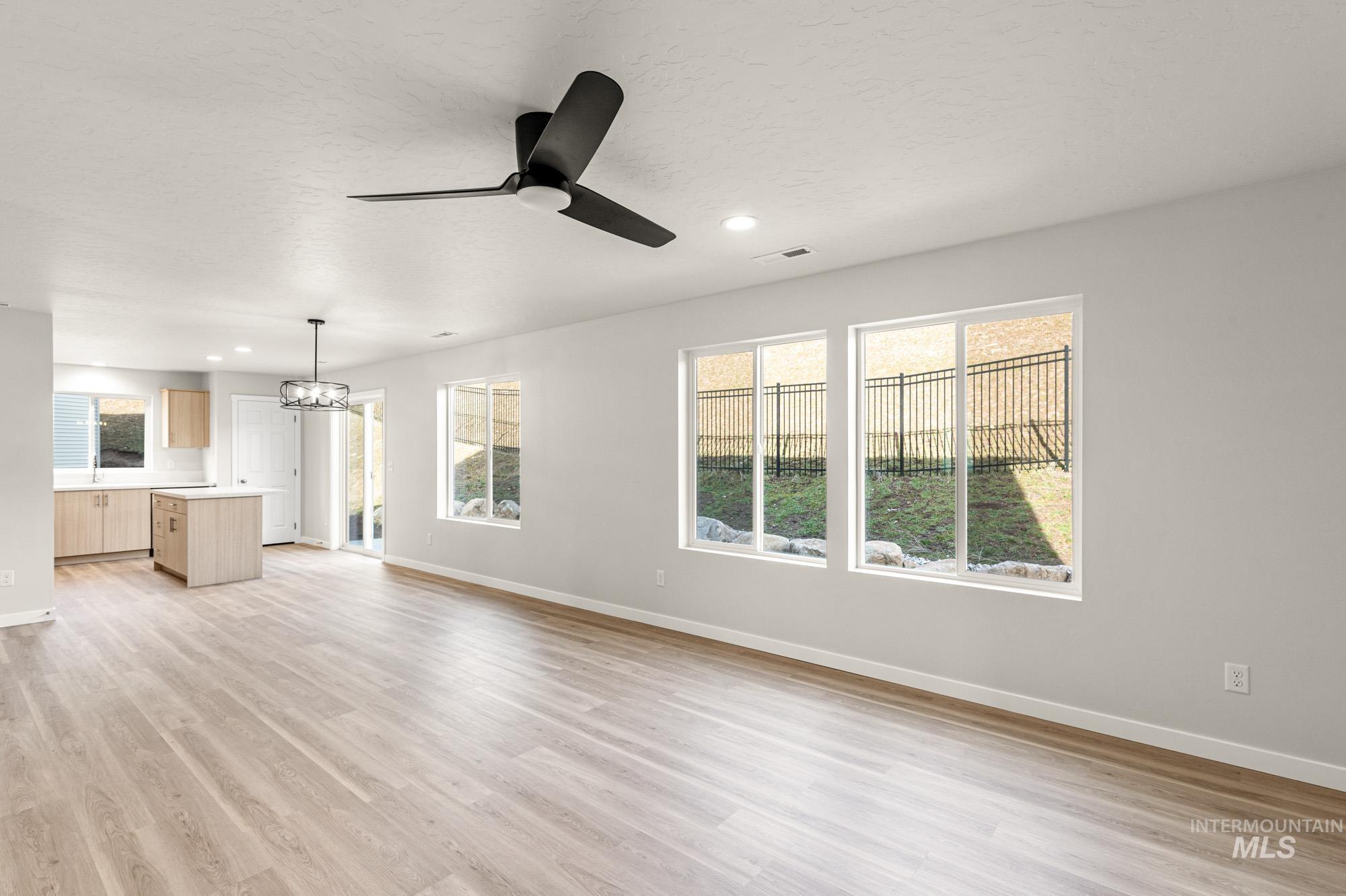 Unfurnished living room featuring a chandelier, ceiling fan, light wood finished floors, and a textured ceiling
