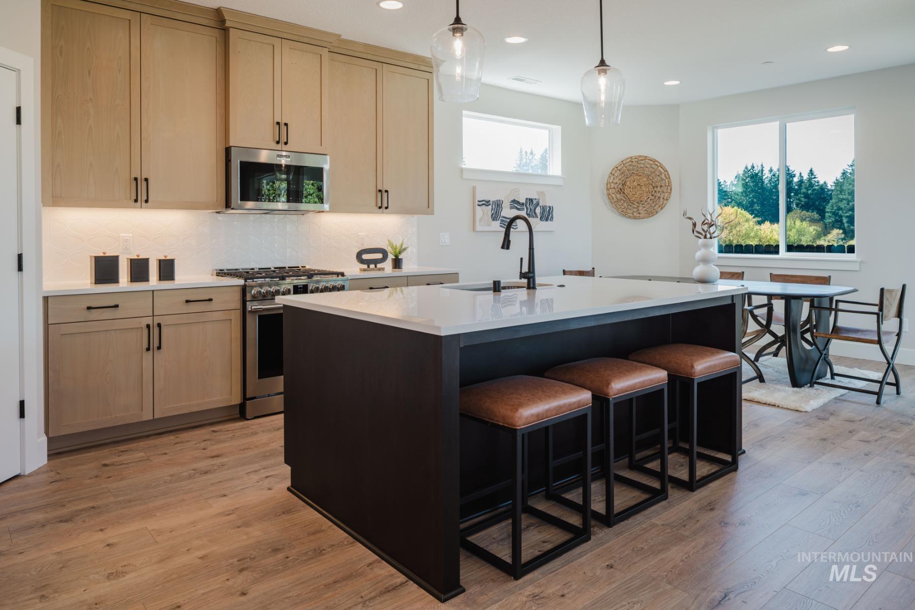 Kitchen featuring stainless steel appliances, decorative backsplash, a kitchen island with sink, pendant lighting, and light wood-style floors