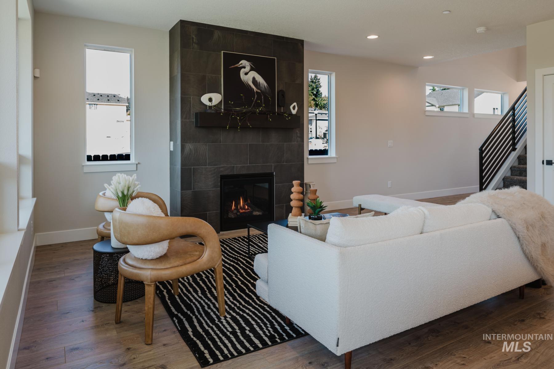 Living area featuring stairway, a tile fireplace, healthy amount of natural light, wood finished floors, and recessed lighting