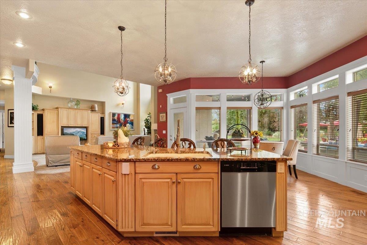 Kitchen with dishwasher, light stone counters, light wood-style flooring, a textured ceiling, and hanging light fixtures