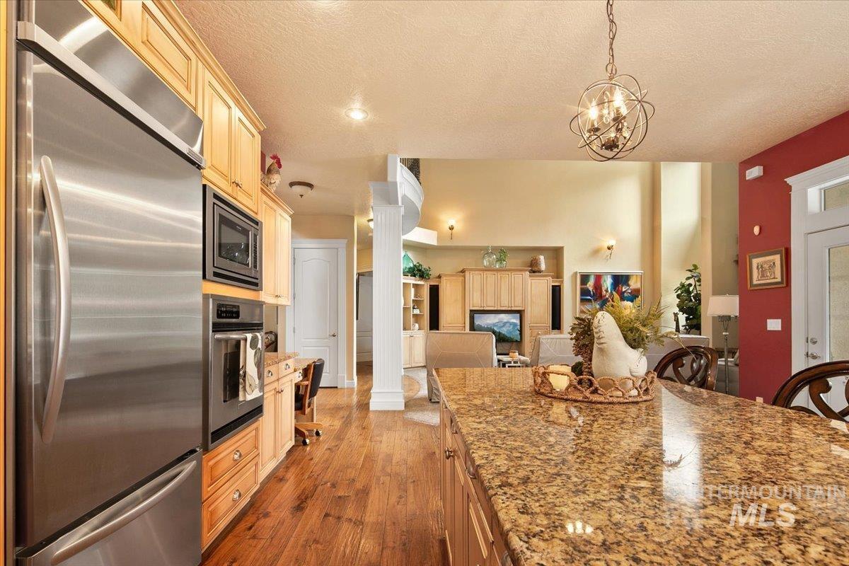 Kitchen featuring stainless steel appliances, light stone counters, dark wood-style floors, a textured ceiling, and hanging light fixtures