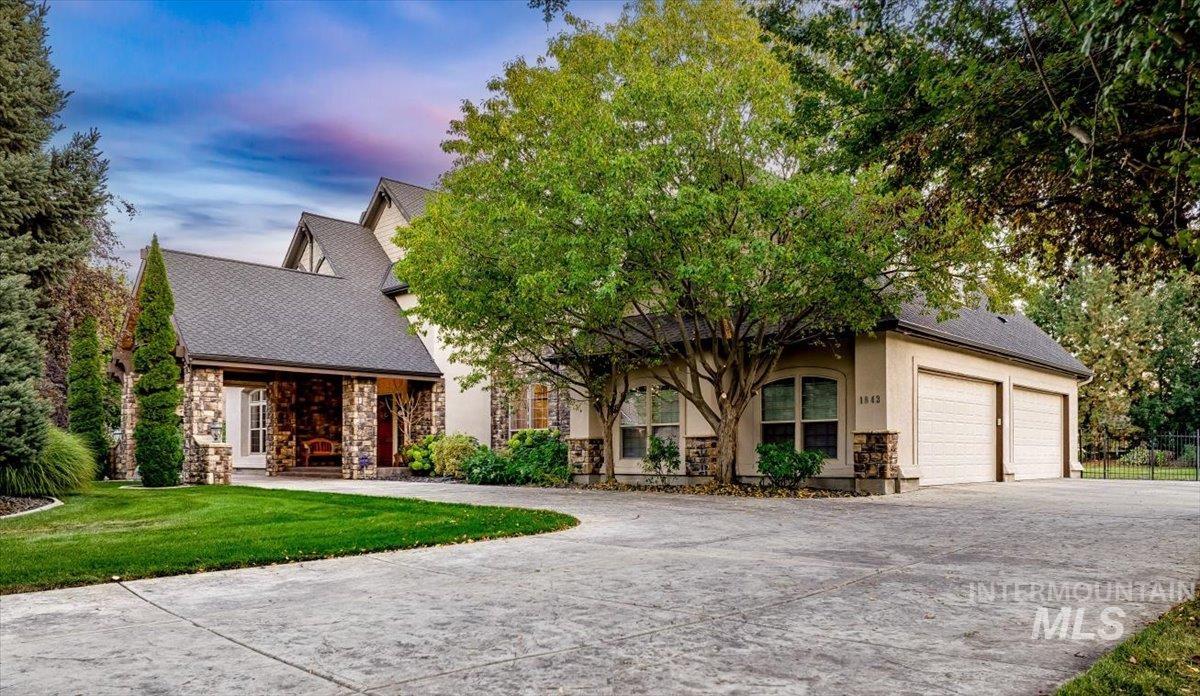 View of front facade with stone siding, driveway, a shingled roof, and a lawn