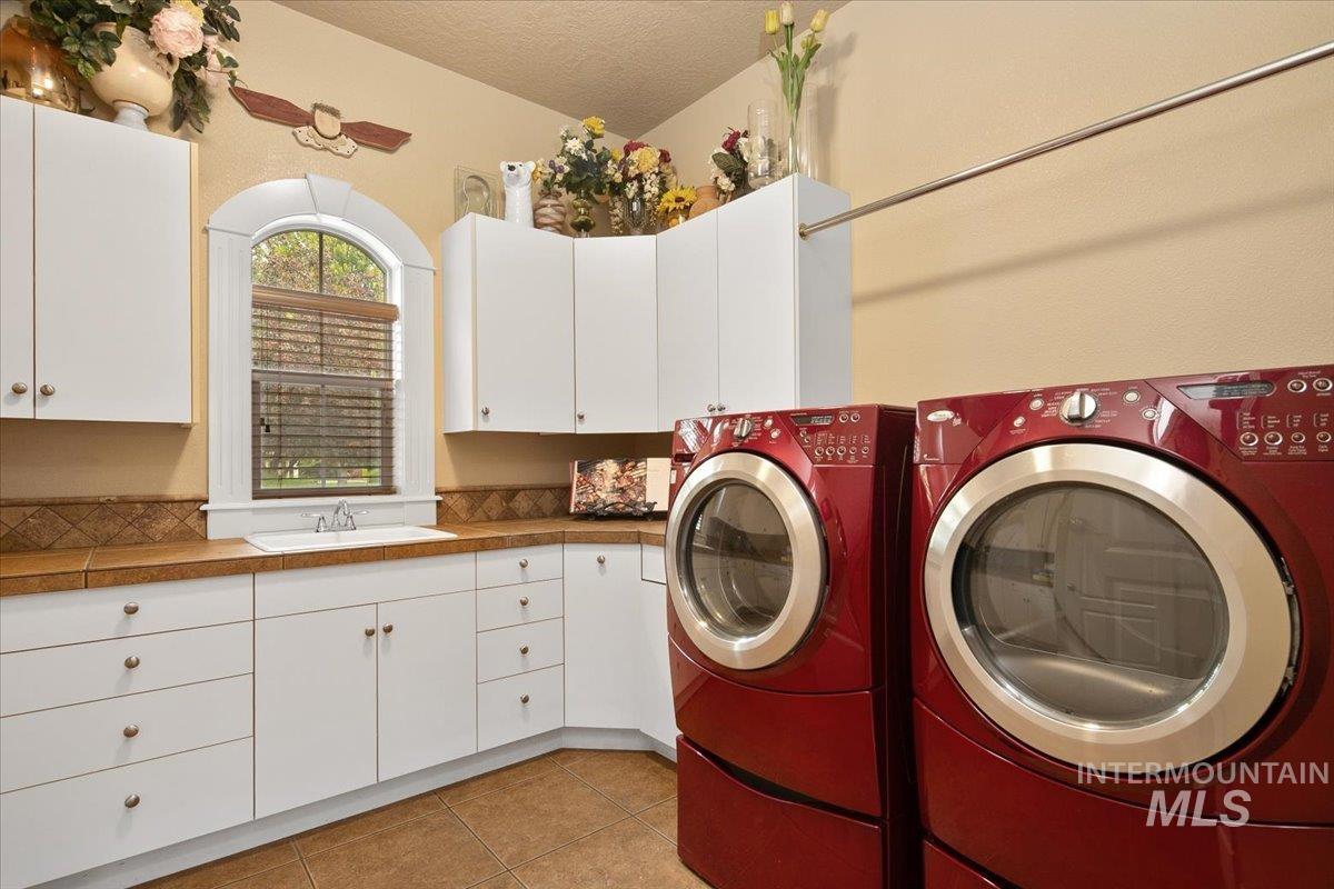 Washroom featuring light tile patterned floors, washing machine and dryer, a textured ceiling, and cabinet space
