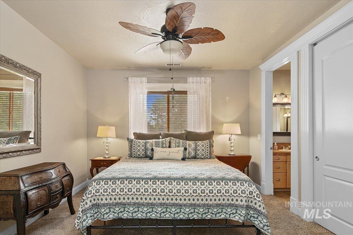 Bedroom with a textured ceiling, light carpet, ceiling fan, and ensuite bathroom