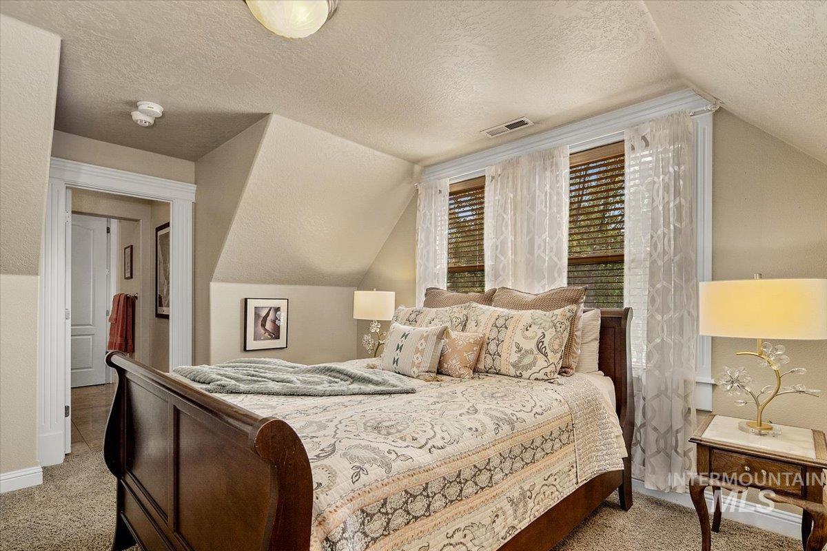 Carpeted bedroom featuring a textured ceiling and vaulted ceiling