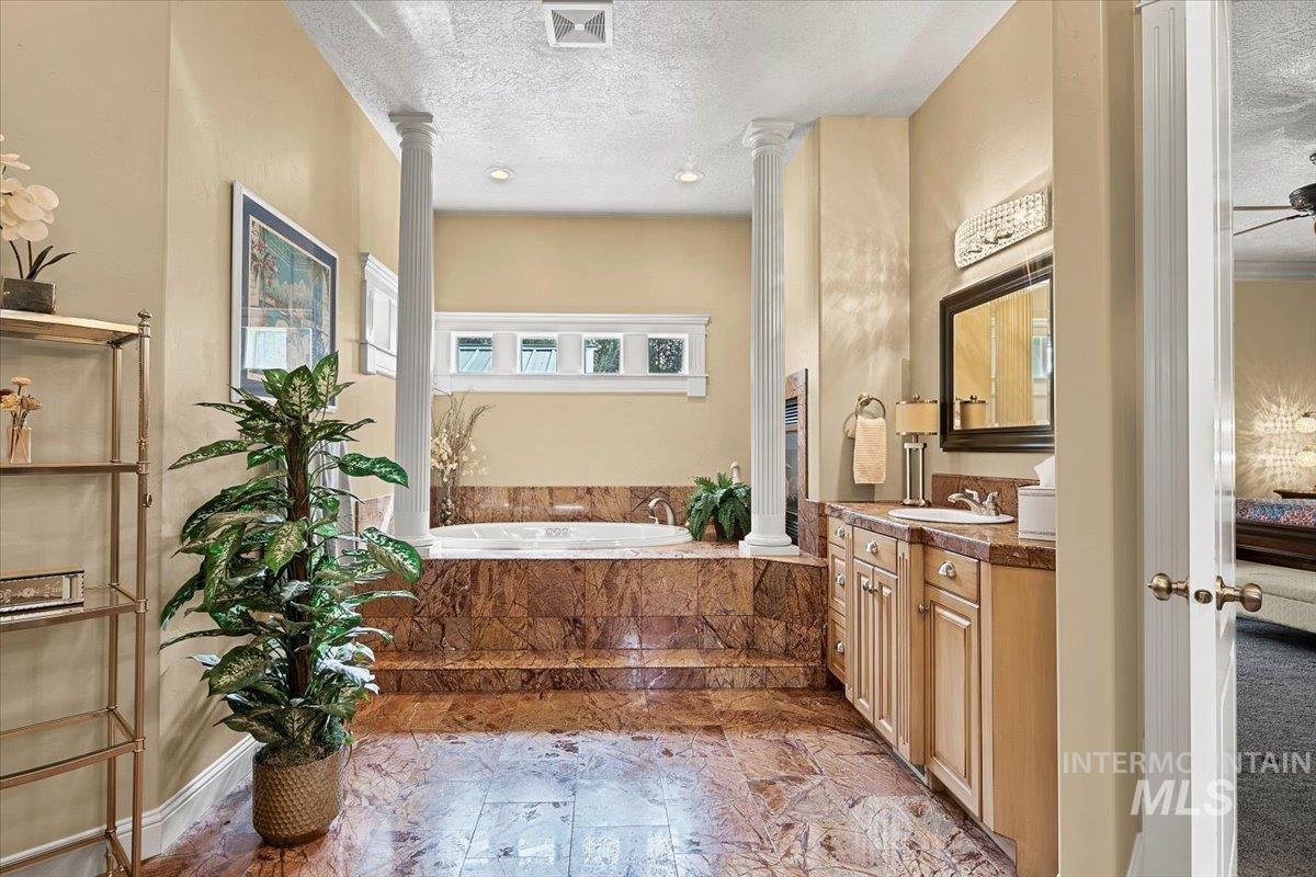Ensuite bathroom with a bath, vanity, a textured ceiling, and decorative columns
