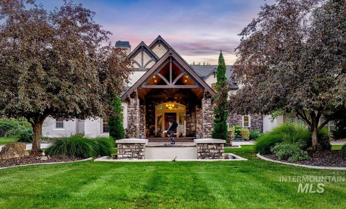 View of front of property with a yard, a chimney, stone siding, and a patio area