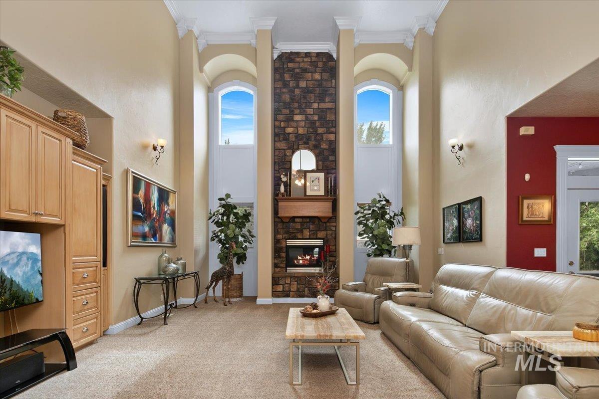 Living room with healthy amount of natural light, light colored carpet, a high ceiling, a stone fireplace, and crown molding