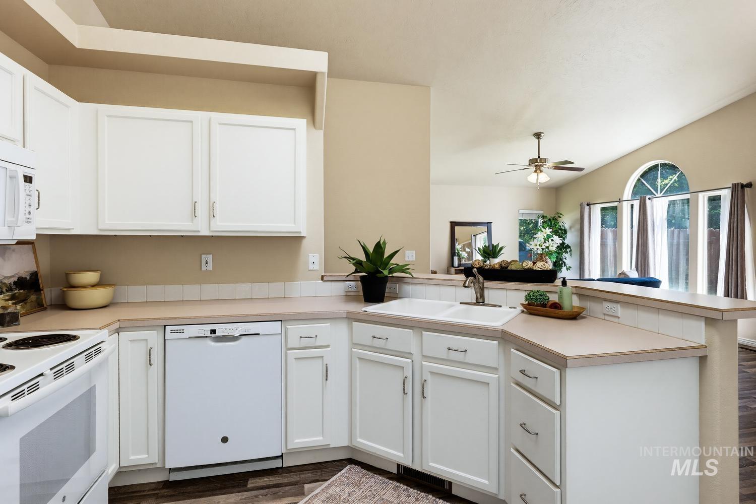 Kitchen featuring white cabinetry, light-toned countertops, a double basin sink with a high-arc faucet, and wood-finish flooring