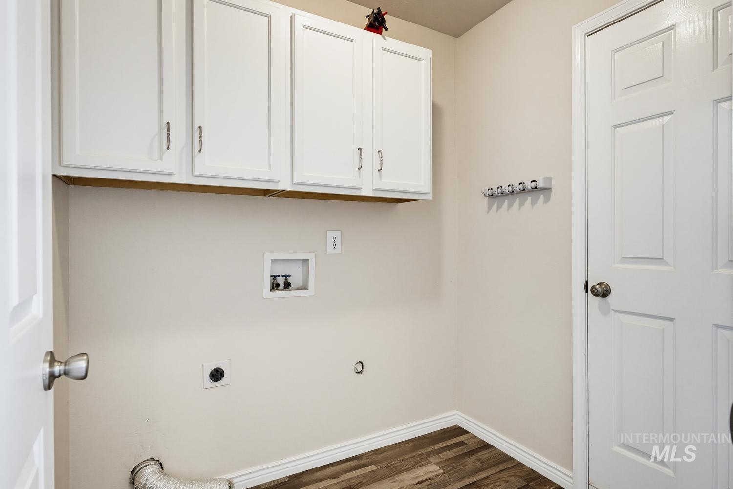 Dedicated laundry area featuring overhead white cabinetry, wood-finish flooring, and a wall-mounted coat rack
