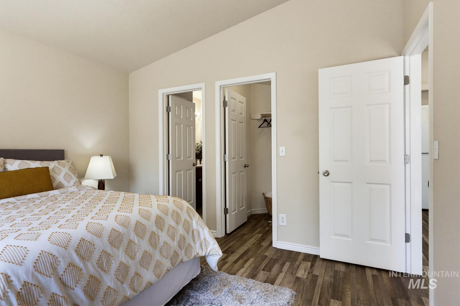 Bedroom featuring vaulted ceilings, wood-finish flooring, and multiple six-panel doors