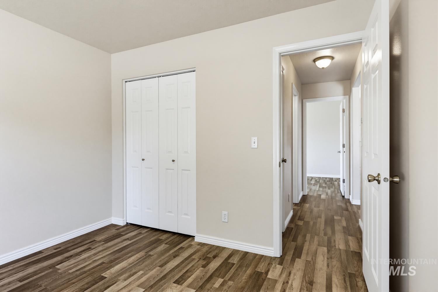 Room featuring wood-finish flooring, light neutral-toned walls, and white baseboards