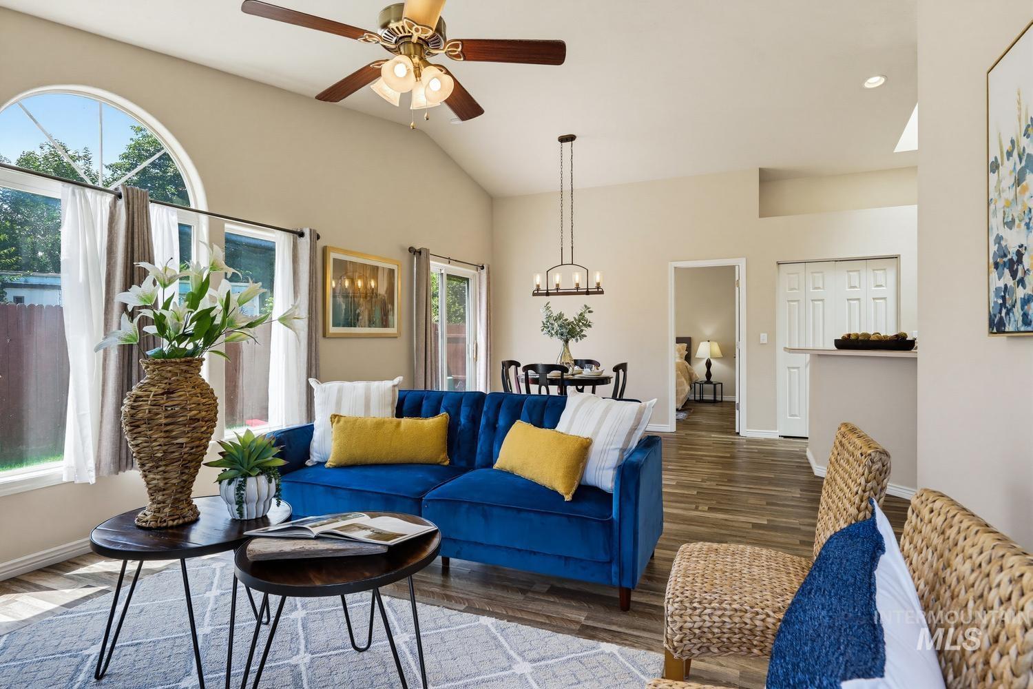 Vaulted ceilings with a ceiling fan, arched window, wood-finish flooring, a contemporary chandelier, and a breakfast bar