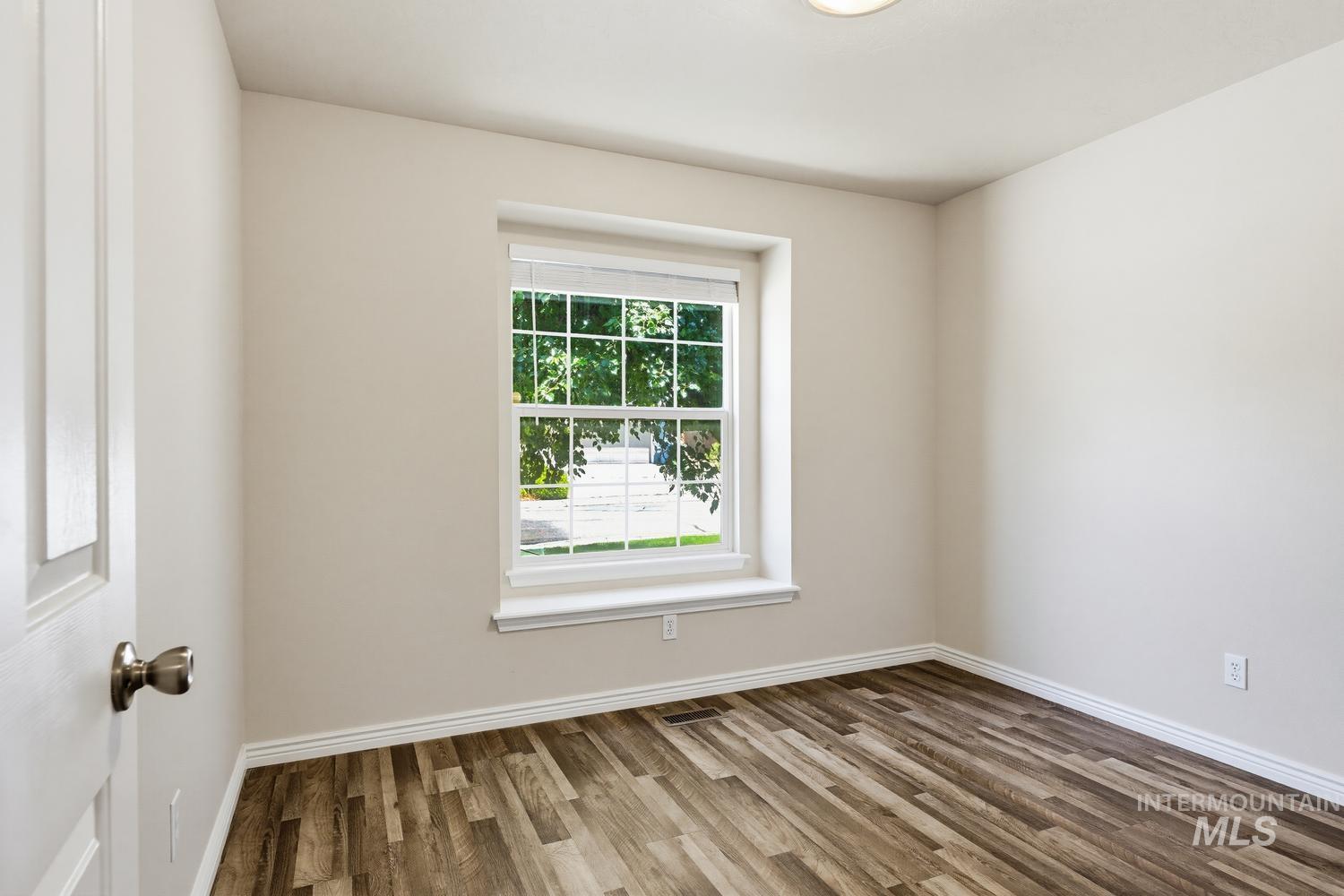 Room featuring a window with blinds, wood-finish flooring, white baseboards, and a flush-mount ceiling light