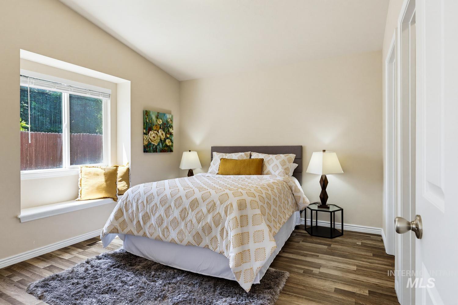 Room featuring wood-finish flooring, a window with a built-in sill seat, and a vaulted ceiling