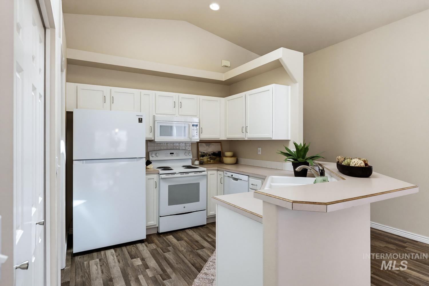 Kitchen featuring white cabinetry and appliances, wood-finish flooring, a double basin sink, and a multi-level countertop