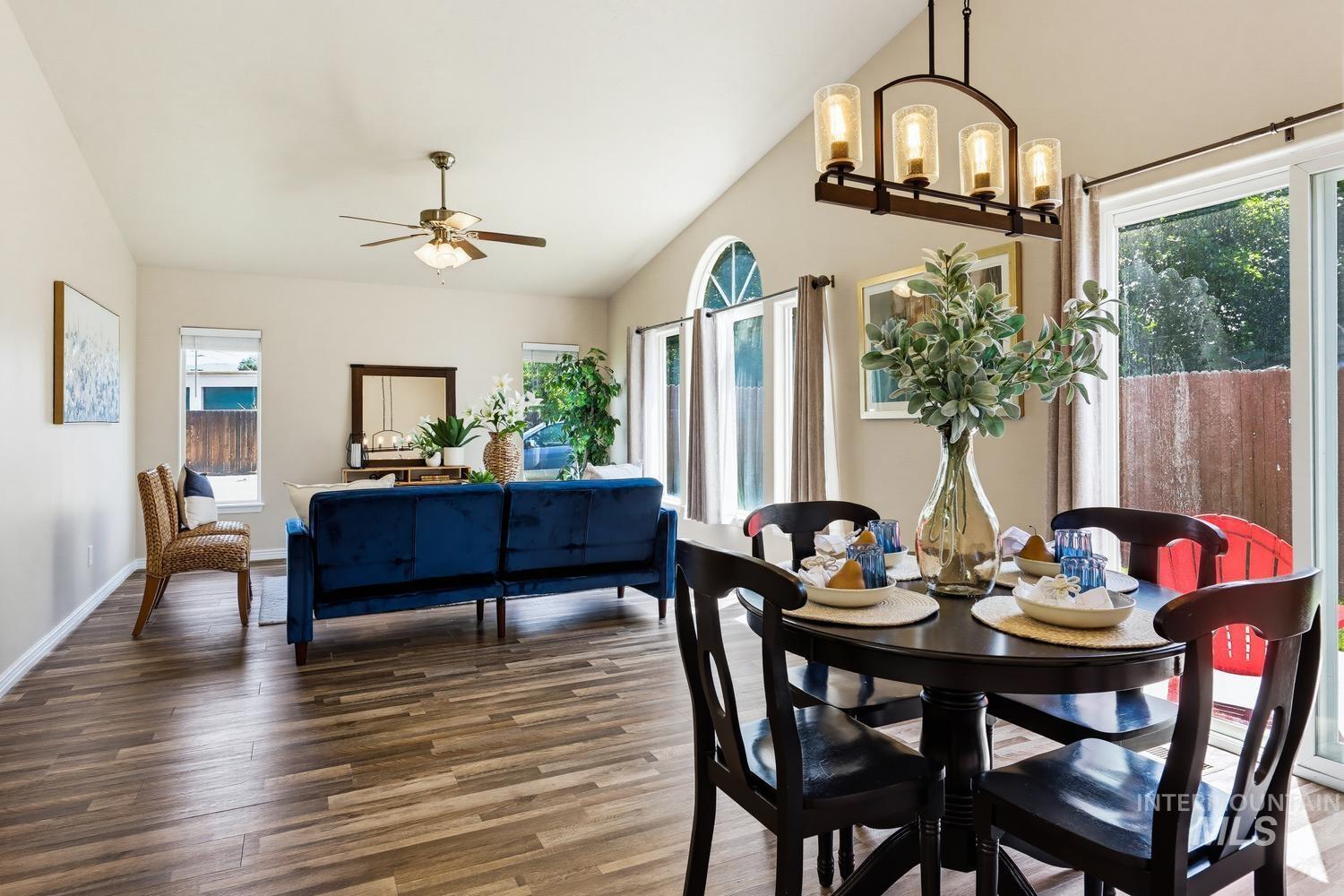 Open-concept living and dining area featuring wood-finish flooring, vaulted ceilings, and a ceiling fan
