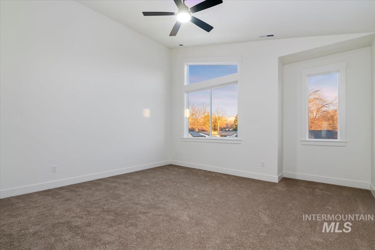 Unfurnished room with dark colored carpet, ceiling fan, and lofted ceiling