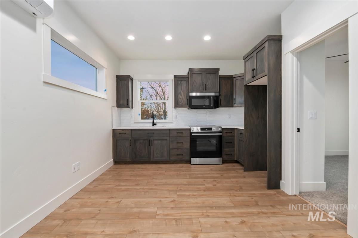 Kitchen with light countertops, appliances with stainless steel finishes, dark brown cabinets, decorative backsplash, and light wood-type flooring