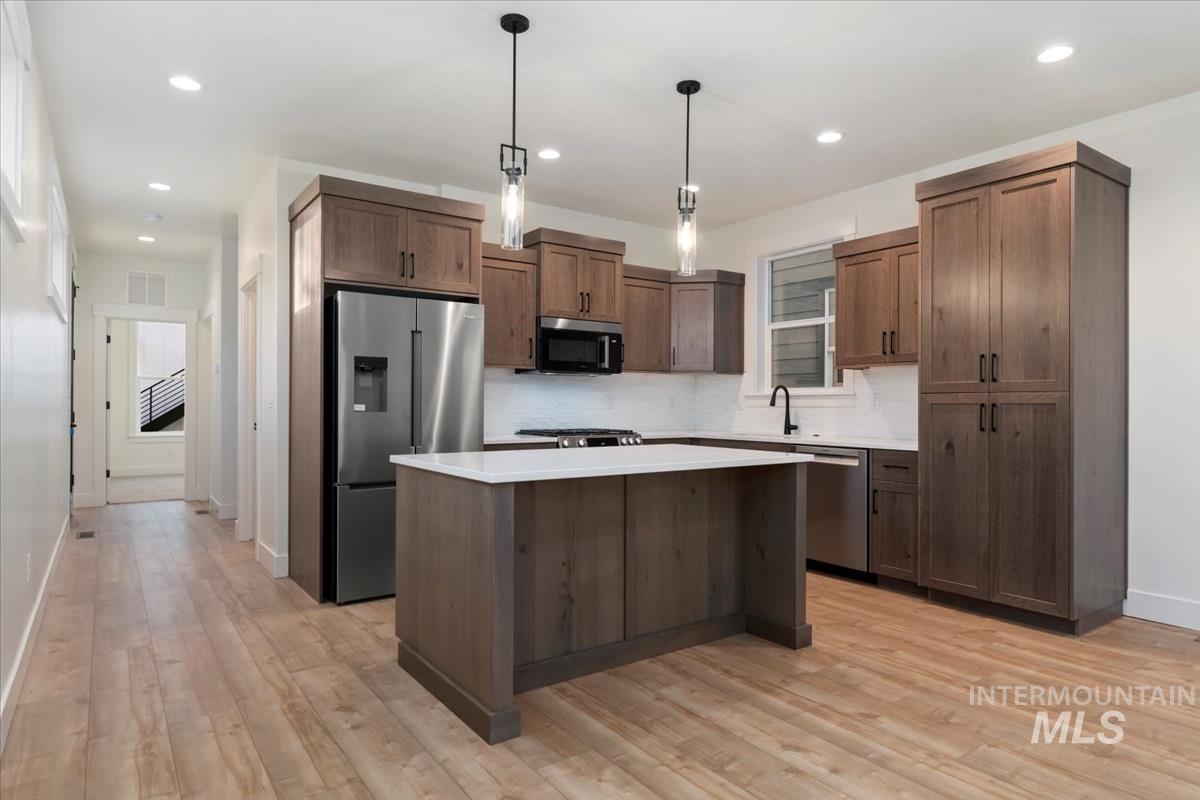 Kitchen with hanging light fixtures, a center island, appliances with stainless steel finishes, backsplash, and recessed lighting