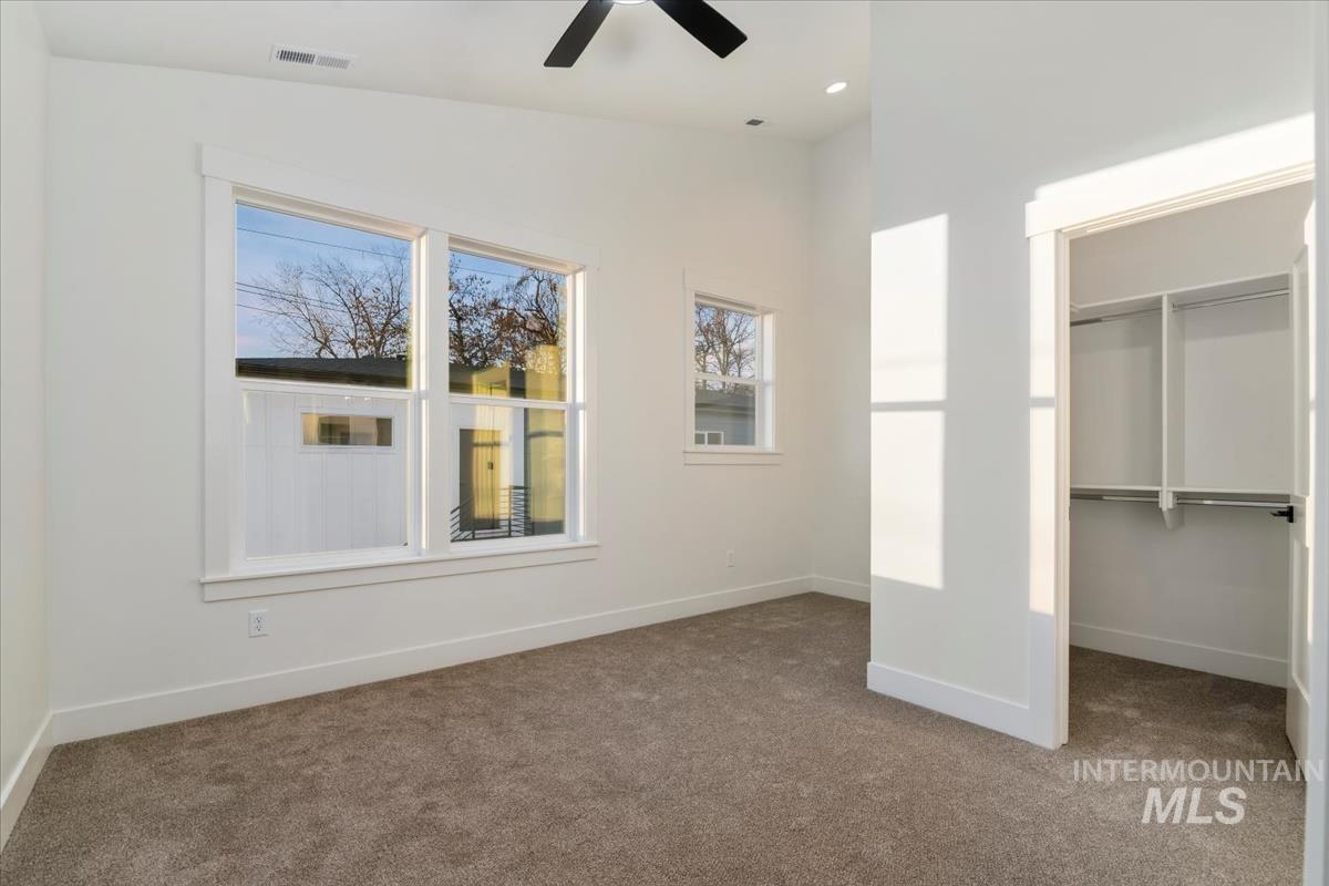 Unfurnished bedroom with multiple windows, carpet floors, a walk in closet, ceiling fan, and vaulted ceiling