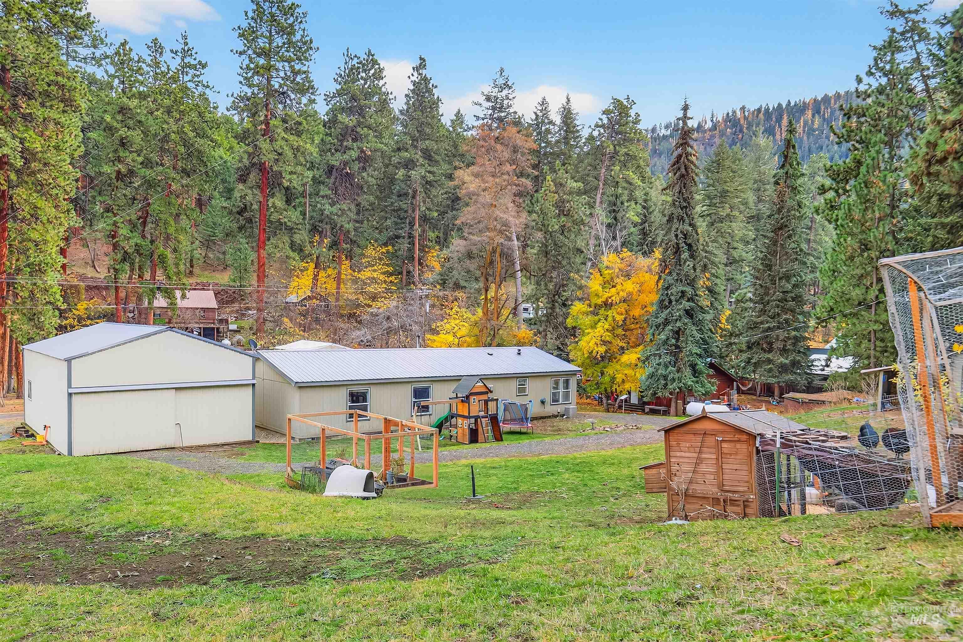 Rear view of property featuring an outdoor structure, a playground, a lawn, and a view of trees