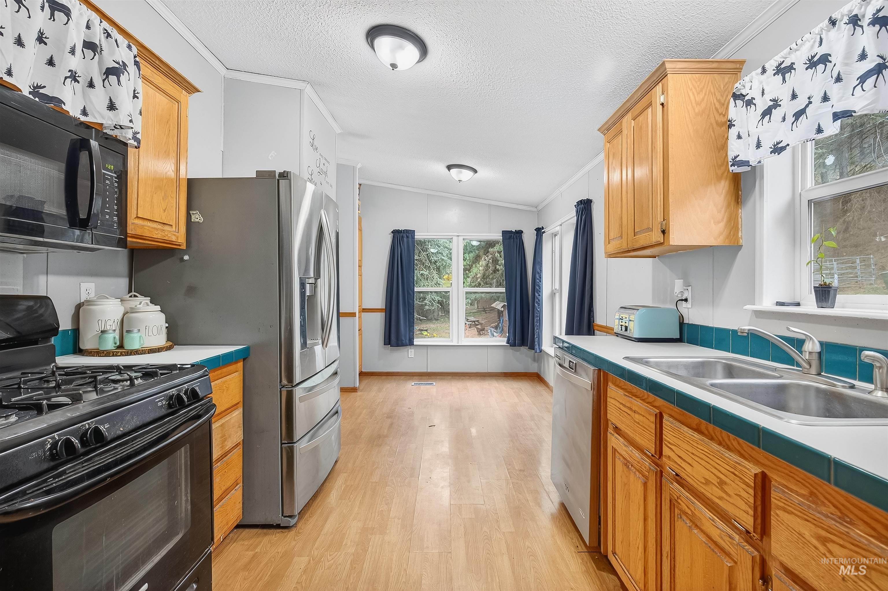 Kitchen featuring black appliances, brown cabinetry, a textured ceiling, light wood finished floors, and crown molding