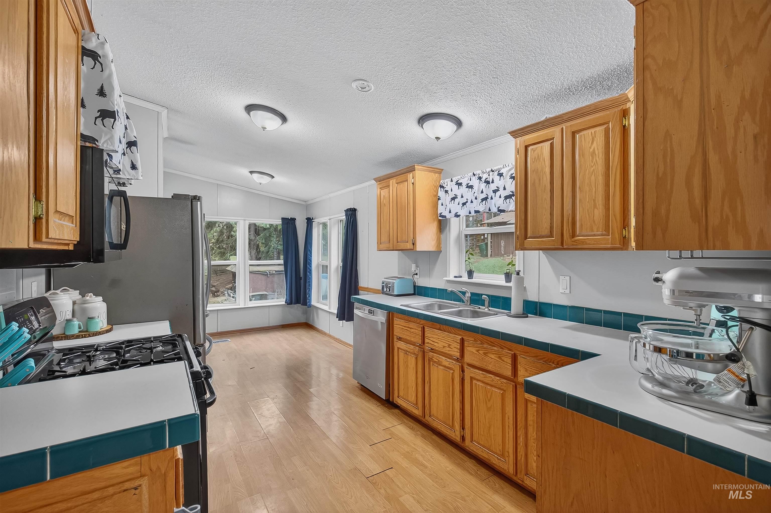 Kitchen featuring black gas stove, healthy amount of natural light, light wood finished floors, brown cabinets, and a textured ceiling