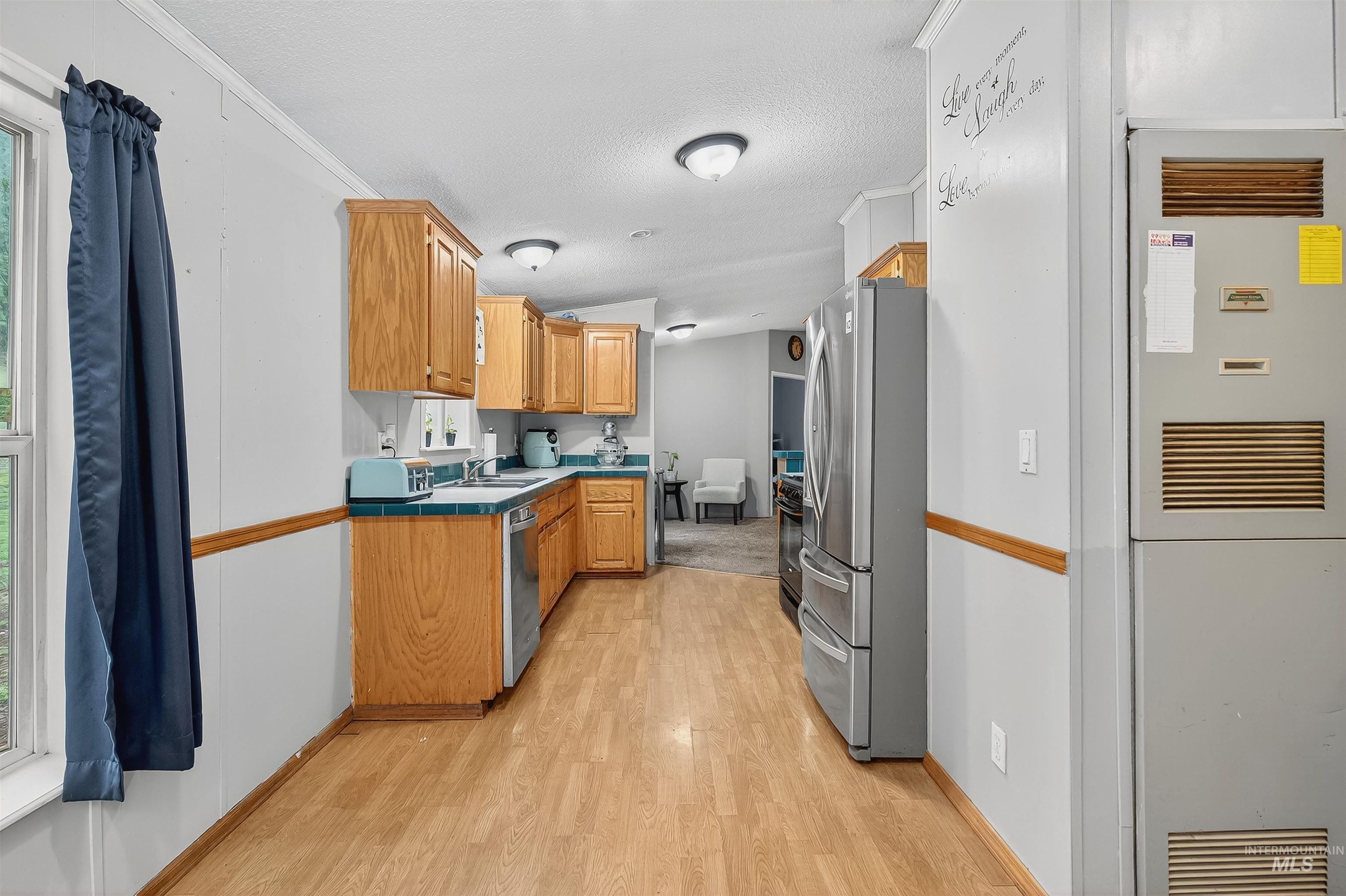 Kitchen featuring a heating unit, light wood finished floors, stainless steel appliances, a textured ceiling, and tile countertops