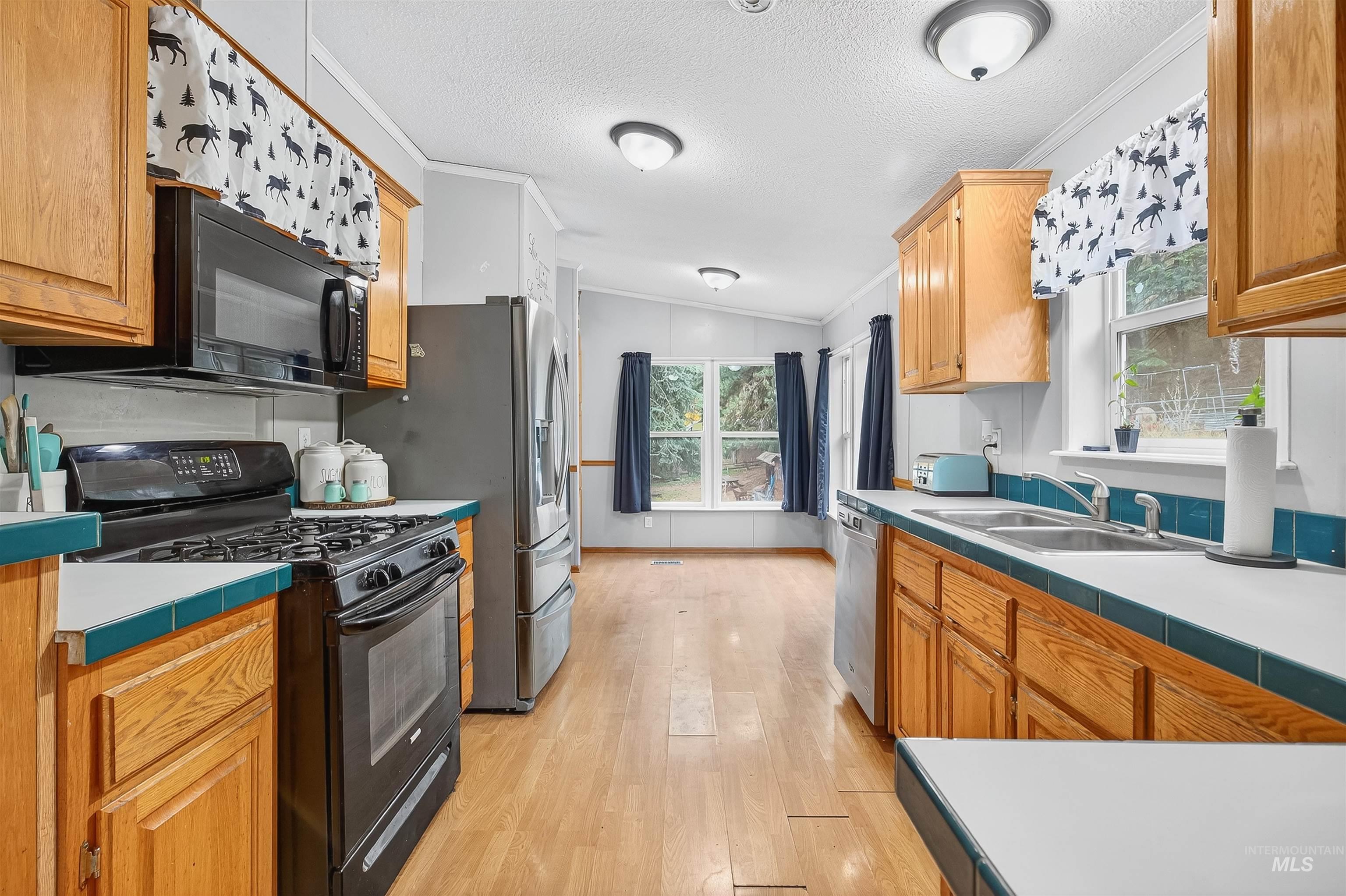 Kitchen with tile countertops, black appliances, a textured ceiling, plenty of natural light, and light wood-type flooring