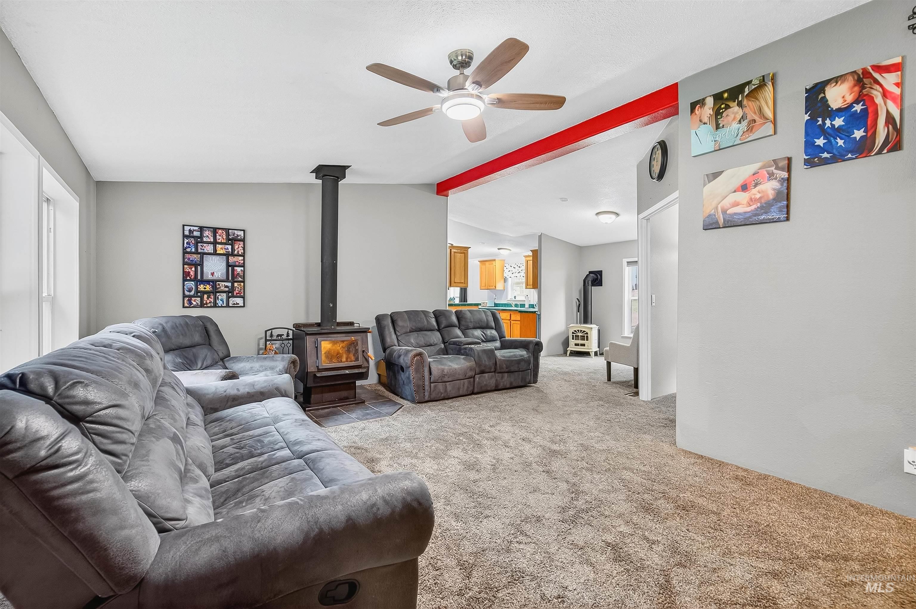 Living area with a wood stove, carpet flooring, and a ceiling fan