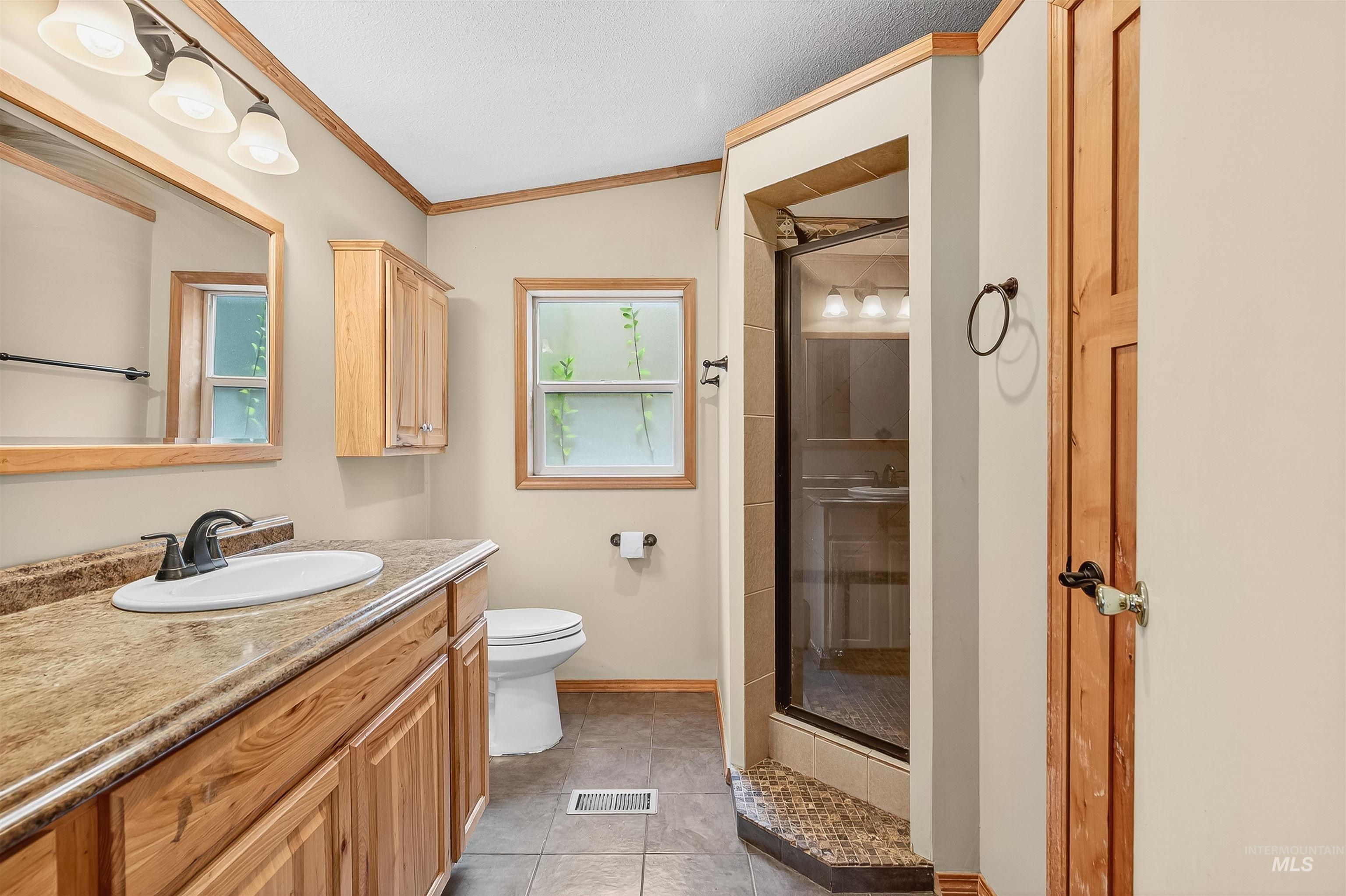 Full bathroom with vanity, a shower stall, crown molding, light tile patterned floors, and lofted ceiling