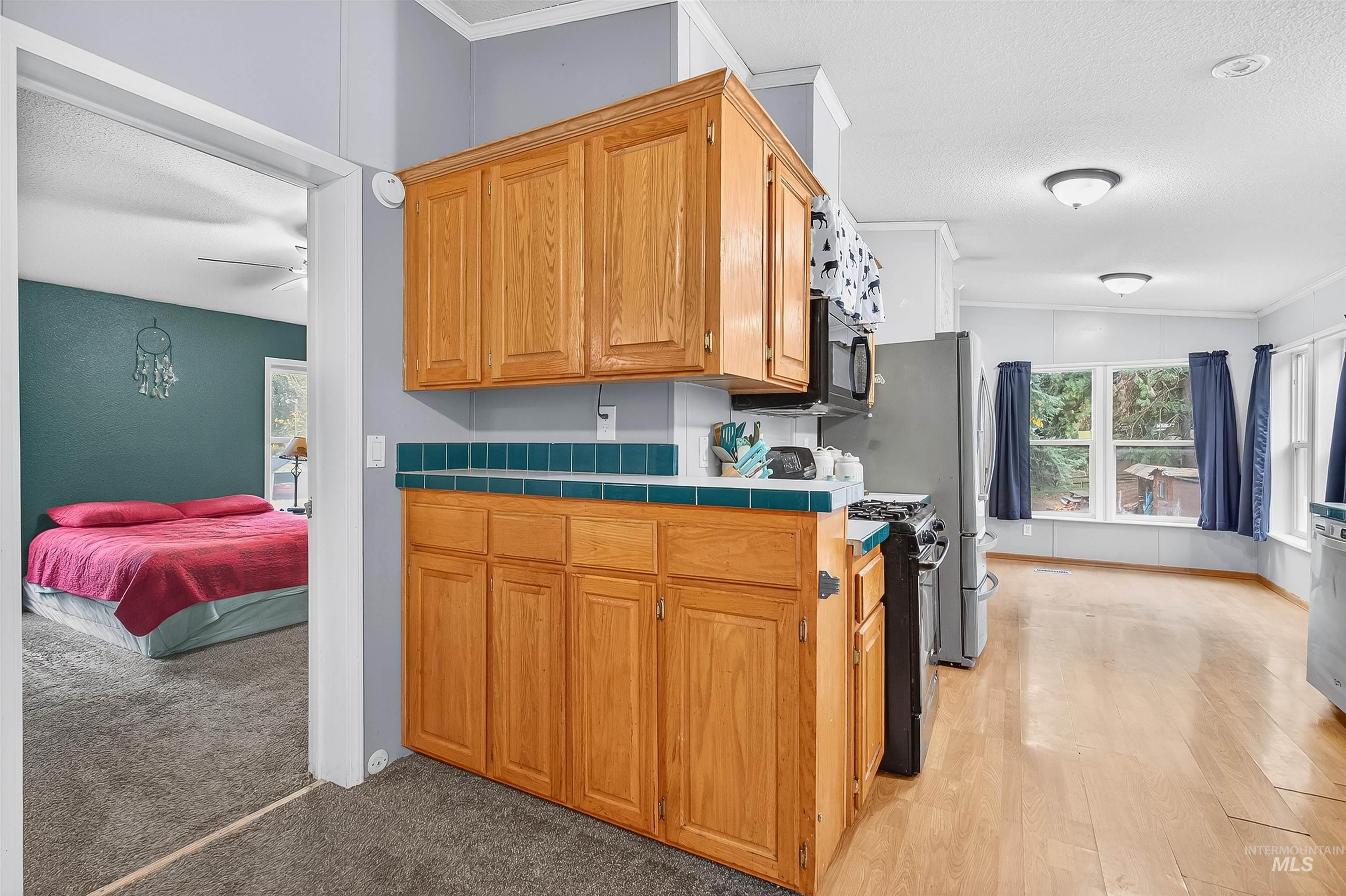 Kitchen featuring black appliances, brown cabinets, a textured ceiling, crown molding, and vaulted ceiling