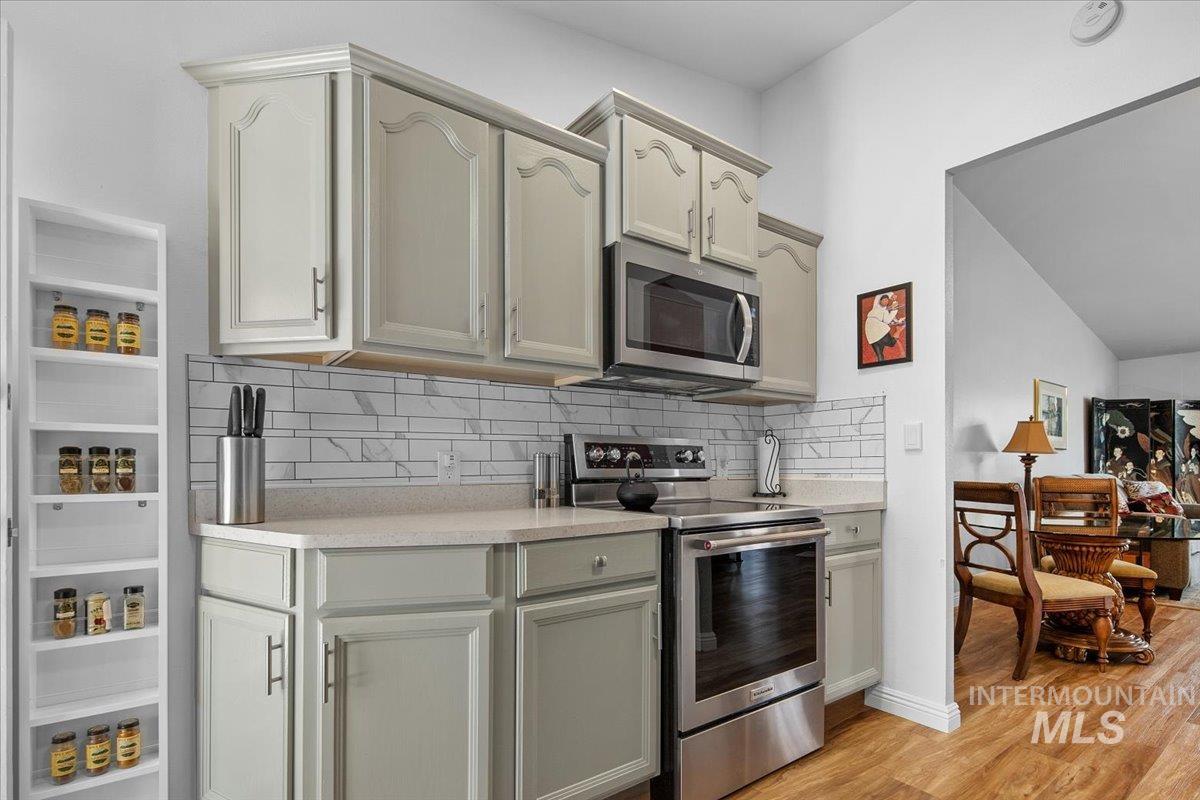 Kitchen featuring stainless steel appliances, tasteful backsplash, light countertops, light wood-type flooring, and vaulted ceiling