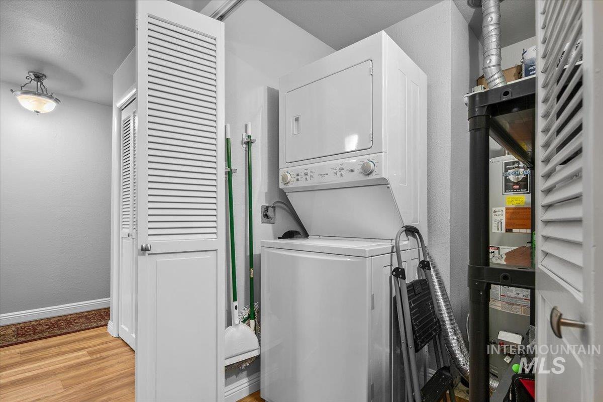 Laundry area featuring light wood-style floors, stacked washer and clothes dryer, heating unit, and a textured wall