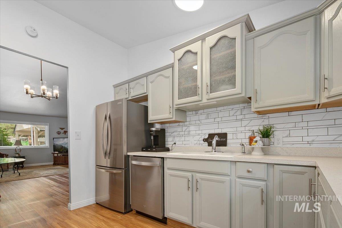 Kitchen with decorative backsplash, stainless steel appliances, light wood-type flooring, light countertops, and hanging light fixtures