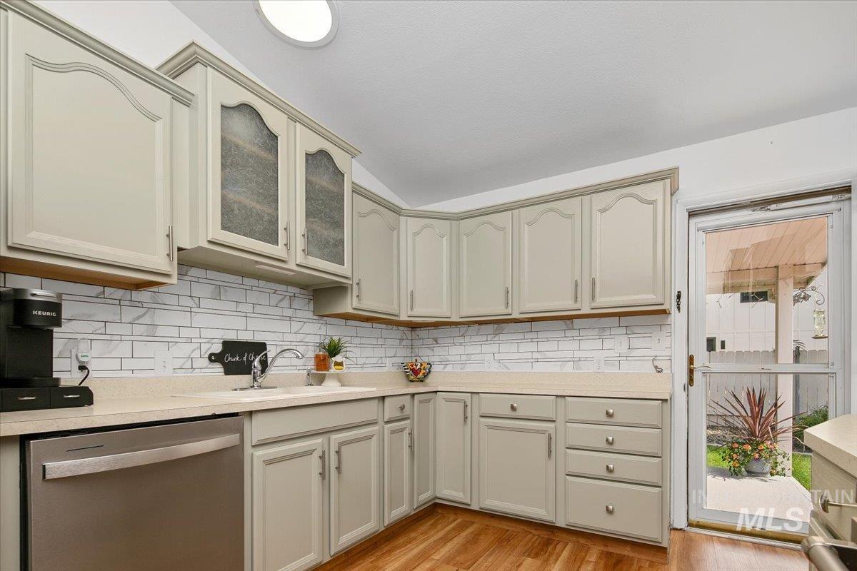 Kitchen featuring dishwasher, light wood-type flooring, light countertops, decorative backsplash, and glass insert cabinets