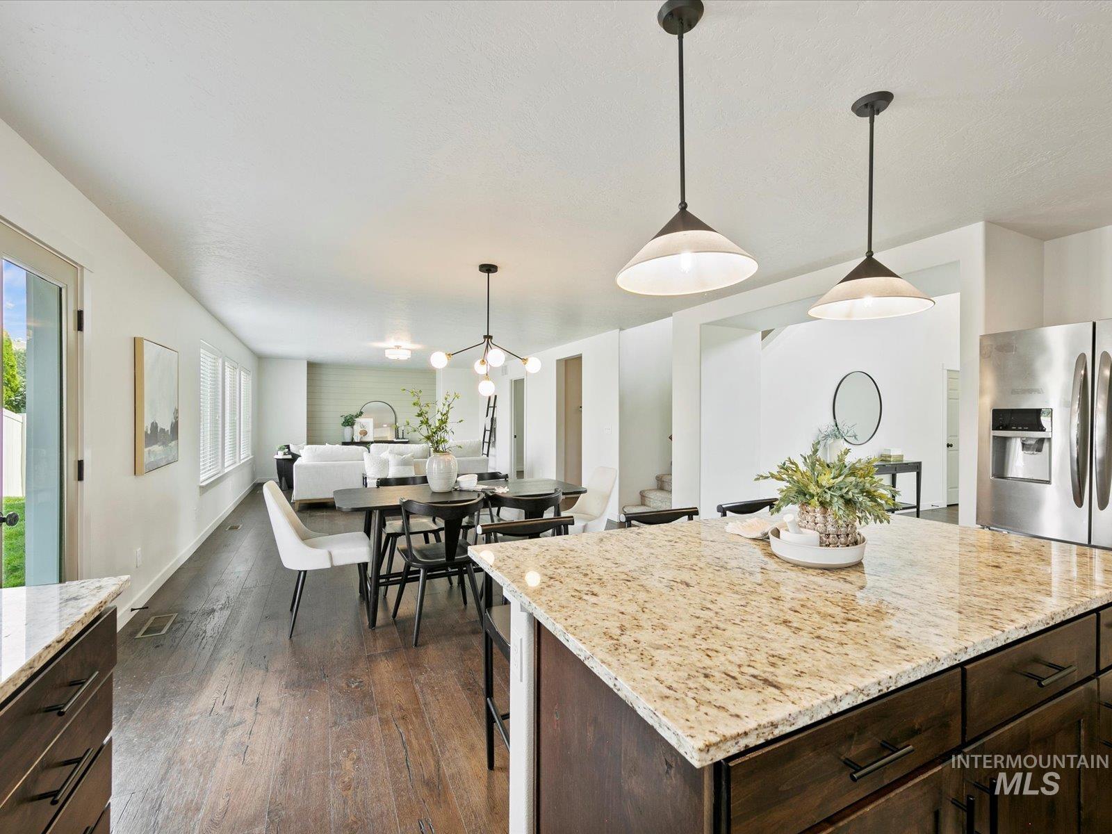 Kitchen featuring dark brown cabinets, light stone counters, decorative light fixtures, dark wood finished floors, and a breakfast bar
