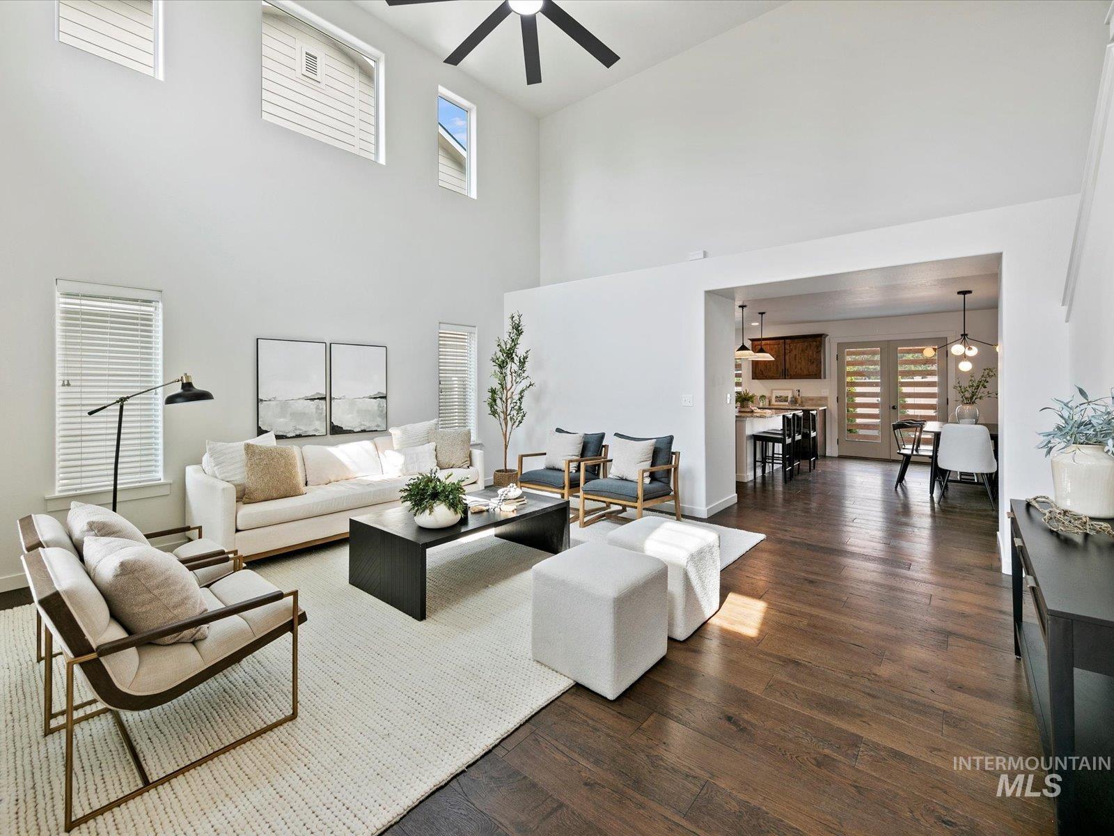 Living room with healthy amount of natural light, dark wood-type flooring, a high ceiling, and a ceiling fan